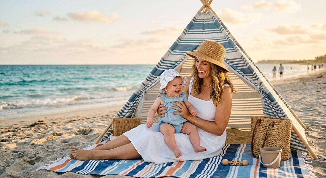 Mère et bébé rieurs sur la plage, sous un tipi rayé, au coucher du soleil.