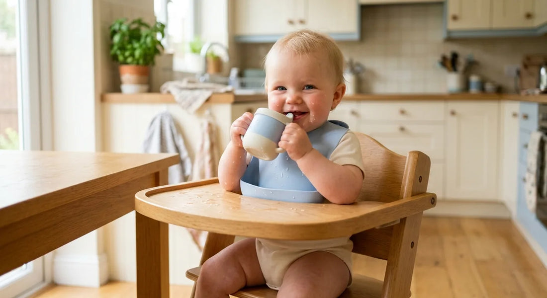 Bébé d'environ dix mois buvant à une tasse d'apprentissage dans sa chaise haute
