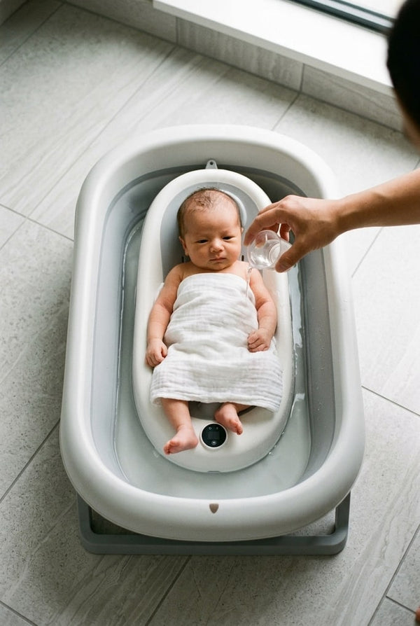 Nouveau-né sur le coussin transat de la baignoire pliante, un lange sur le ventre