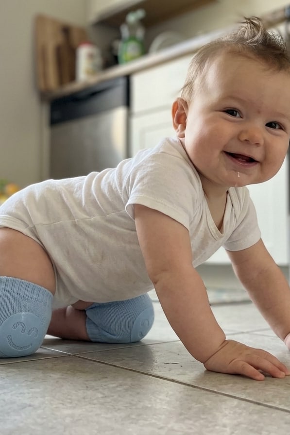 Bébé souriant à quatre pattes sur le carrelage de la cuisine avec ses genouillères
