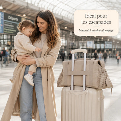 Maman et bébé en gare, sac à langer maternité taupe glissé sur la poignée d'une valise à roulettes